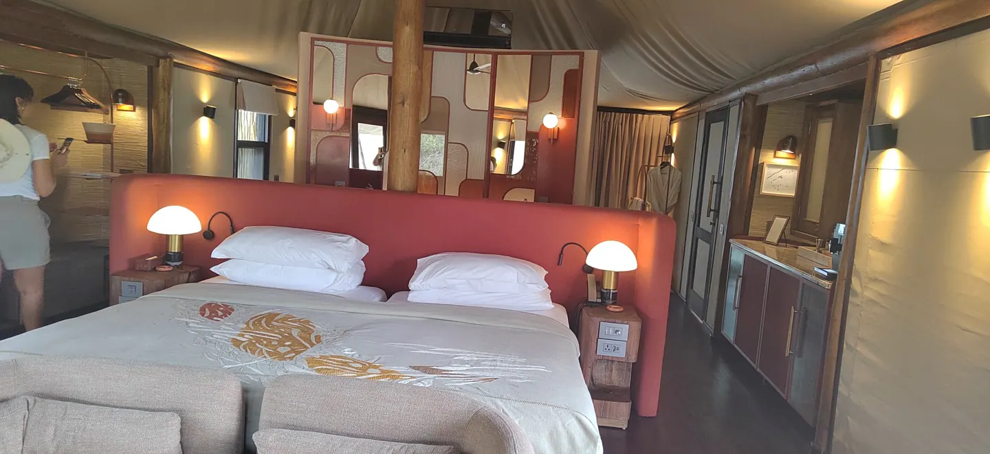 A tented suite with a red headboard, twin lamps and a wide white bed