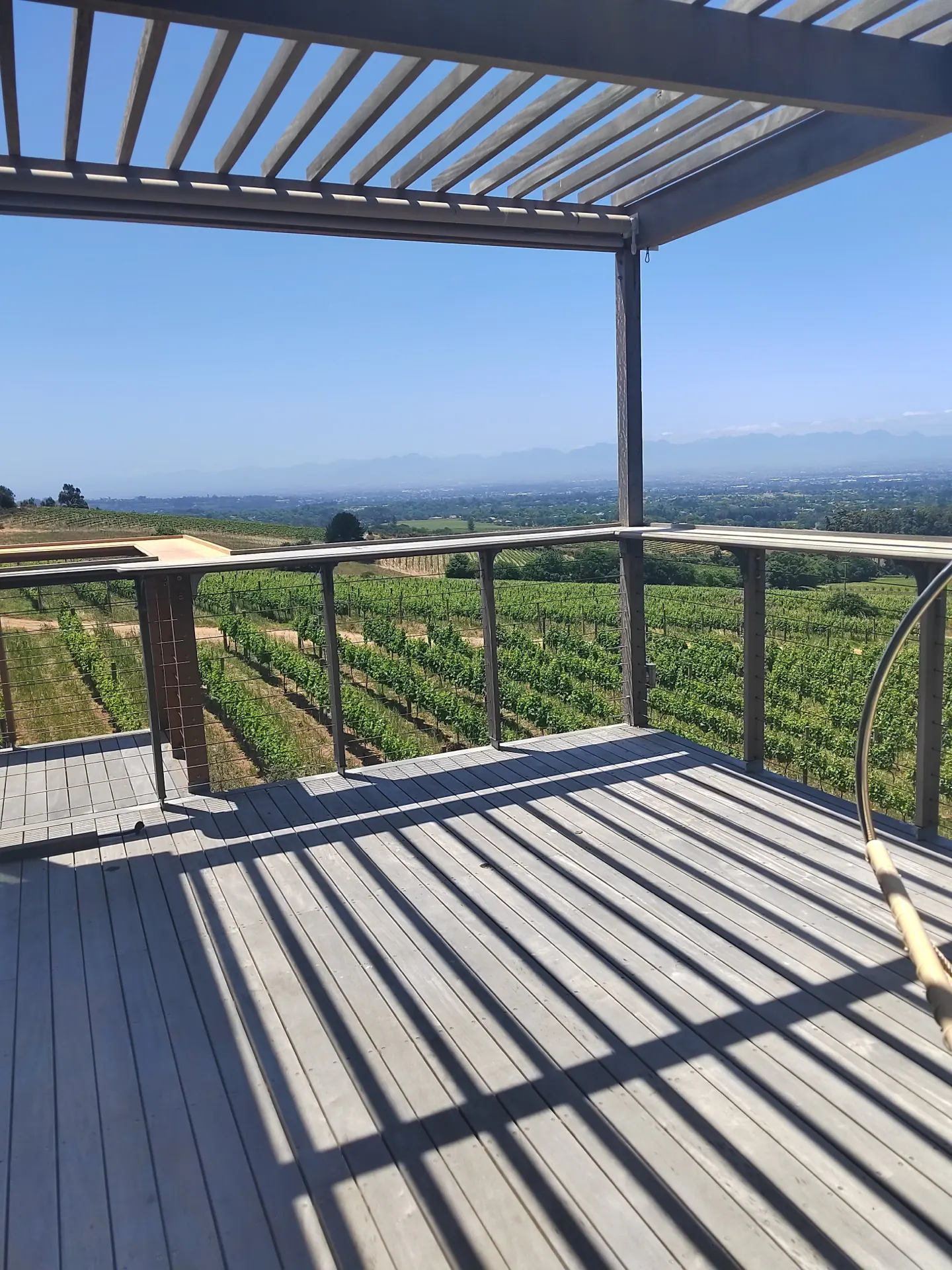Vineyards fall away below a shaded tasting deck, with mountains on the horizon